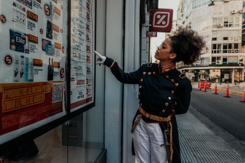 Um indivíduo vestido com roupas históricas interage com a vitrine de uma loja em Buenos Aires, Argentina.